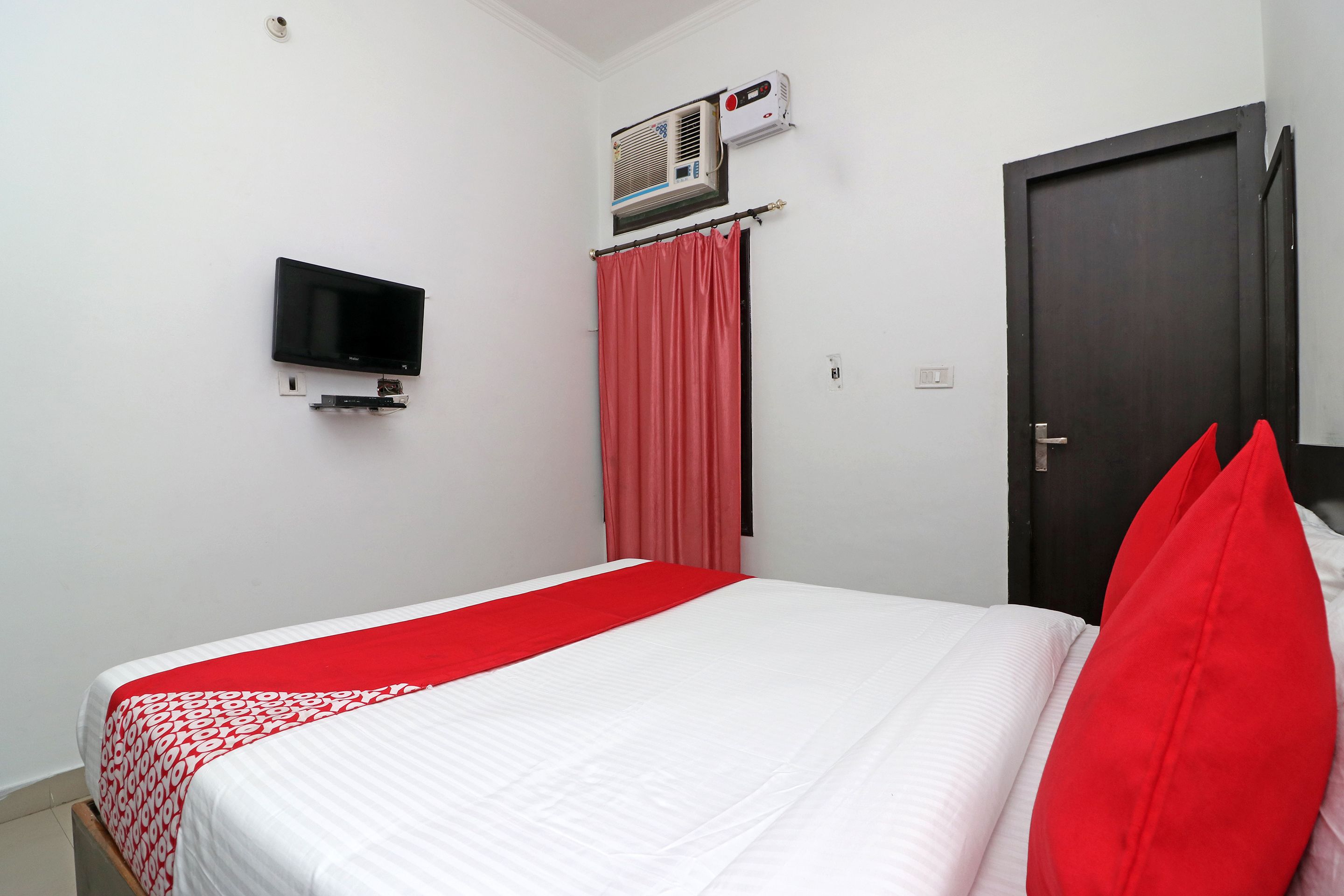 Habitación de hotel con cama, televisor montado en la pared, aire acondicionado y puerta.