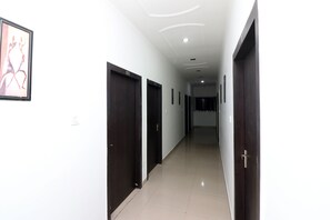 Un pasillo con puertas de madera oscura, paredes blancas y una obra enmarcada a la izquierda.