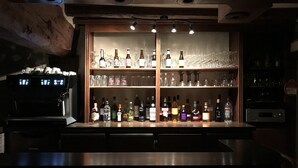 Zona de bar con estantes de botellas de licores y vasos, una máquina de café y techo de madera.