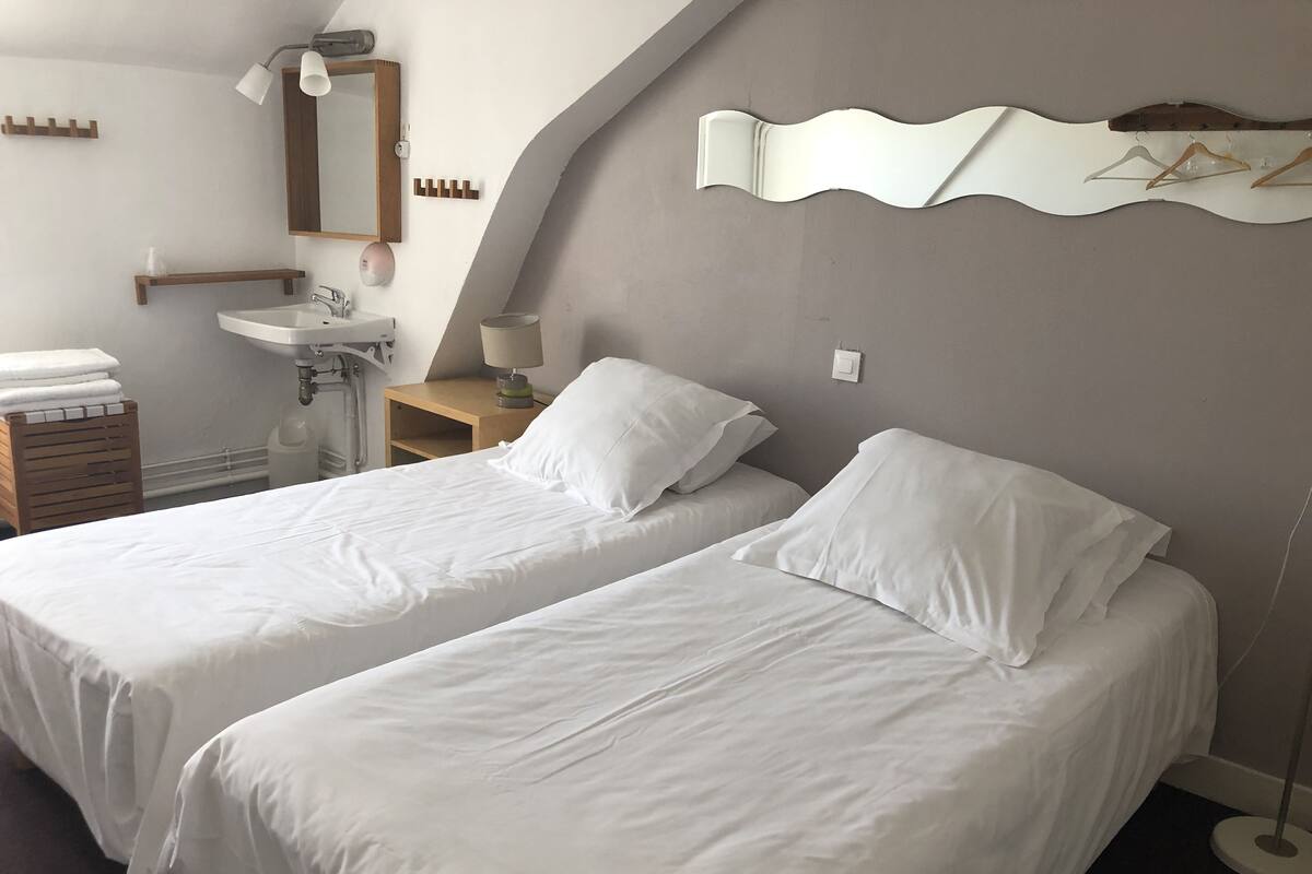 Une chambre avec deux lits, un lavabo, un miroir et un porte-serviettes fixé au mur.
