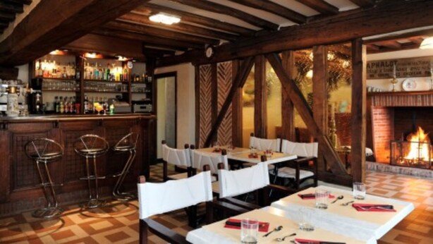 Un restaurante con vigas de madera, una zona de bar con botellas y mesas dispuestas para comer.