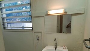 Une salle de bain avec un lavabo blanc, un miroir et une fenêtre avec des stores.