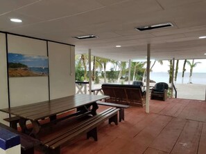 An outdoor patio area with a wooden table and benches, overlooking a beach with palm trees. - Nautica Service Villa Bleue (Point Denis)