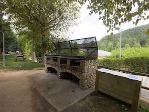 An outdoor grill area with a stone arch structure, a wooden bench, and a picnic table. - Bassegoda Park Campsite (Albanya)
