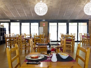 A restaurant with wooden tables and chairs, large windows, and a ceiling with hanging lights. - Bassegoda Park Campsite (Albanya)