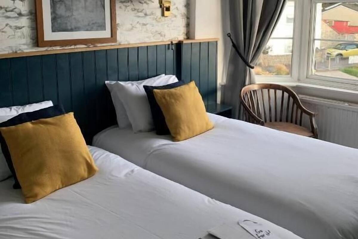 Ein Hotelzimmer mit zwei Betten, einem gerahmten Bild an der Wand, einer Lampe und Blick durch ein Fenster nach draußen.