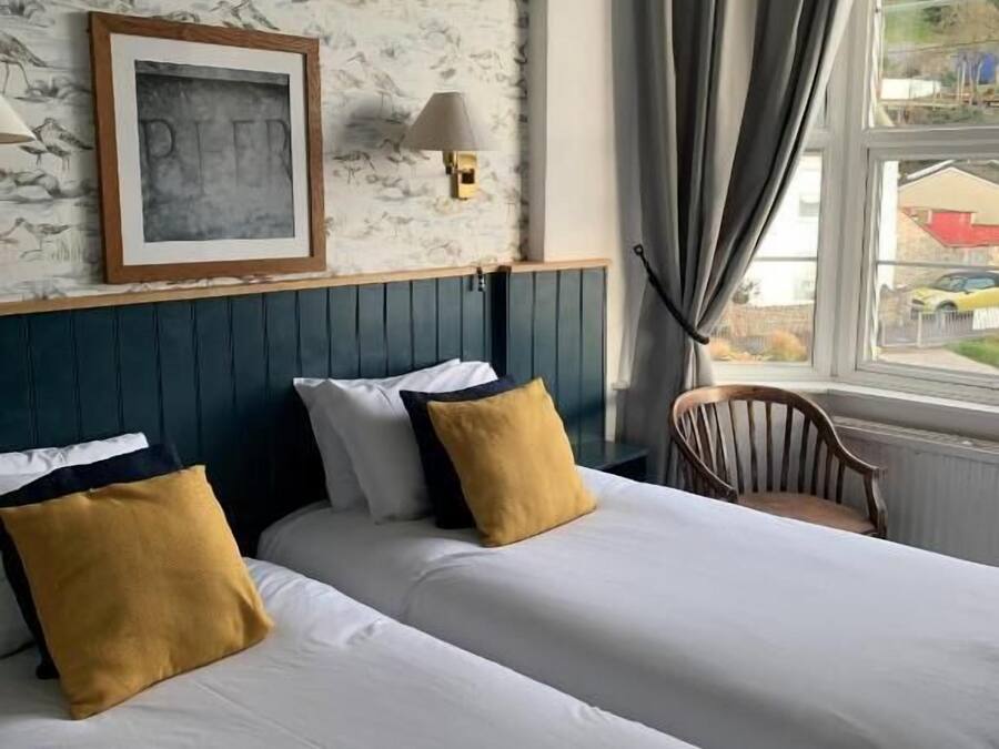 Une chambre d’hôtel avec deux lits, un tableau encadré au mur, une lampe et une vue sur l’extérieur par une fenêtre.