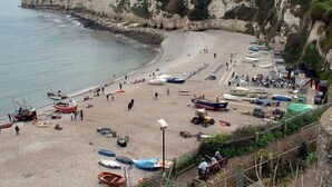 A coastal beach with boats, people, and a cliff. - Anchor Inn by Greene King Inns (Seaton)