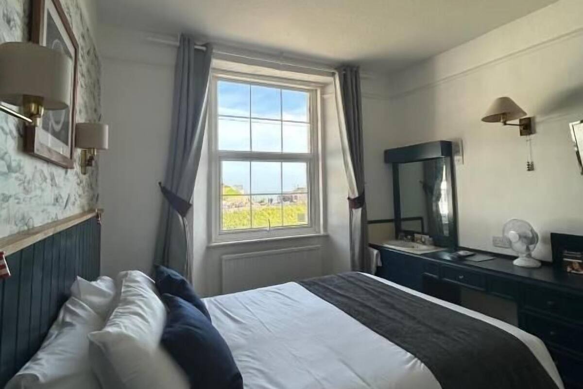 Ein Hotelzimmer mit einem großen Bett, einem Schminktisch, einem Spiegel und einem Fenster mit Vorhängen.