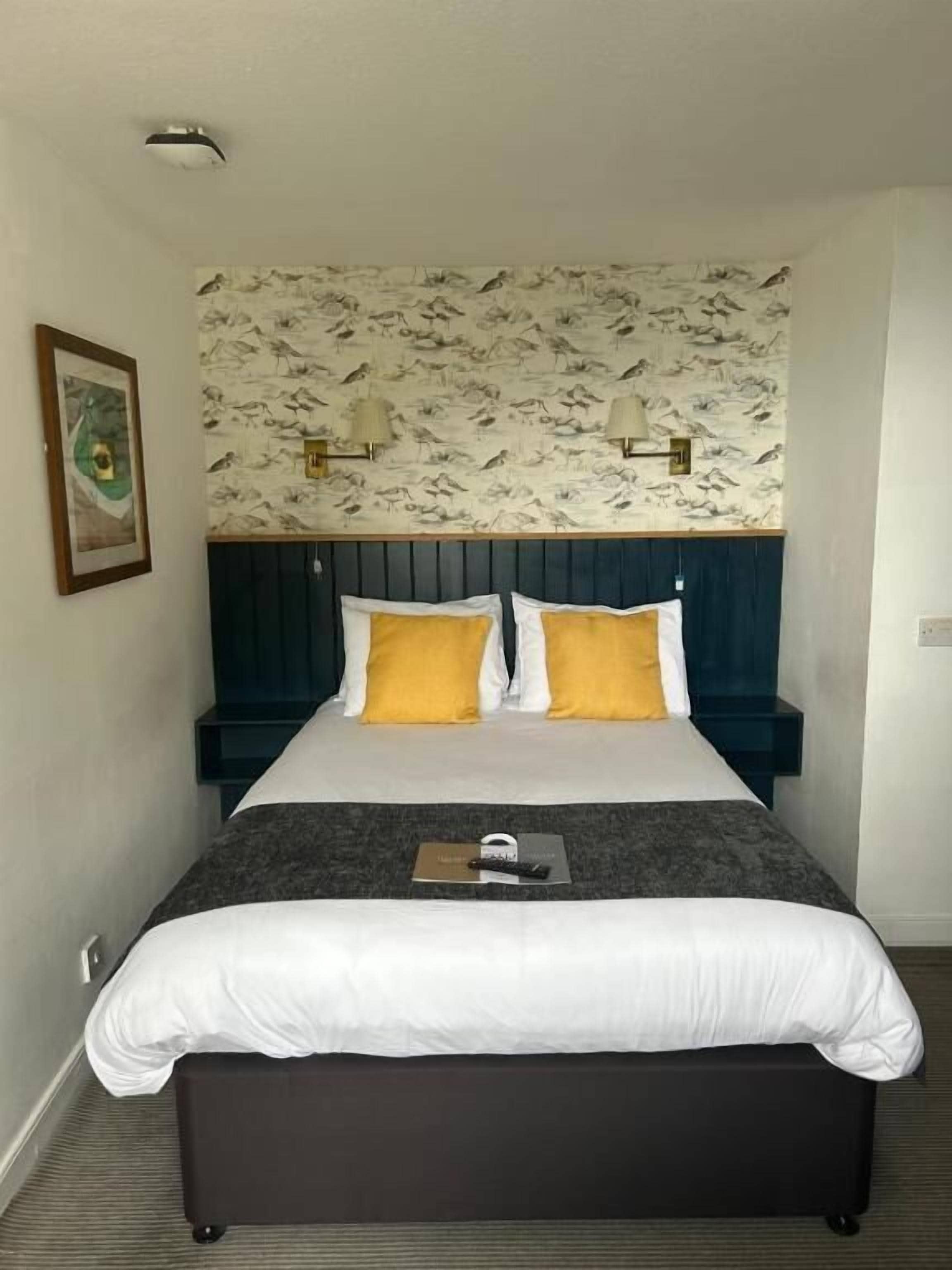 A hotel room with a large bed, two bedside tables, a headboard with a bird pattern wallpaper, and a framed picture on the wall.
