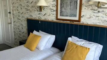 A hotel room with two beds, a framed artwork above the headboard, and wall-mounted lamps.