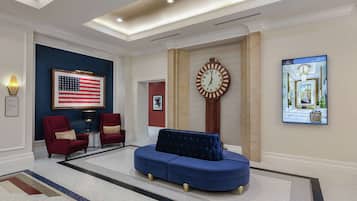 A lobby with a blue sofa, red armchairs, a large American flag, a clock, and a digital display.