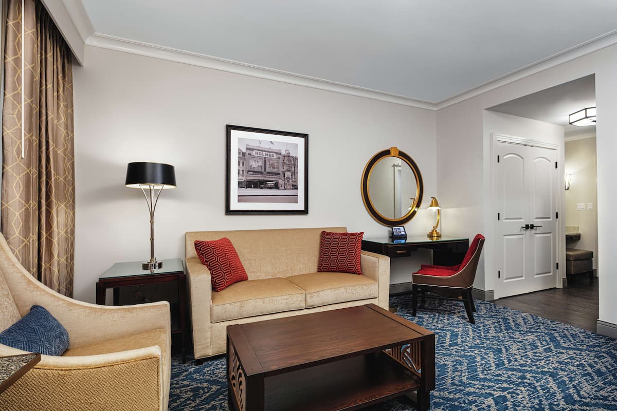 A hotel room with a sofa, armchair, coffee table, and a framed picture on the wall.