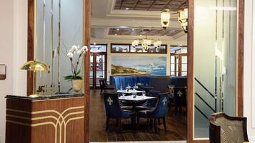 A dining area with a wooden reception desk, blue upholstered chairs, and a view of the ocean through large windows.