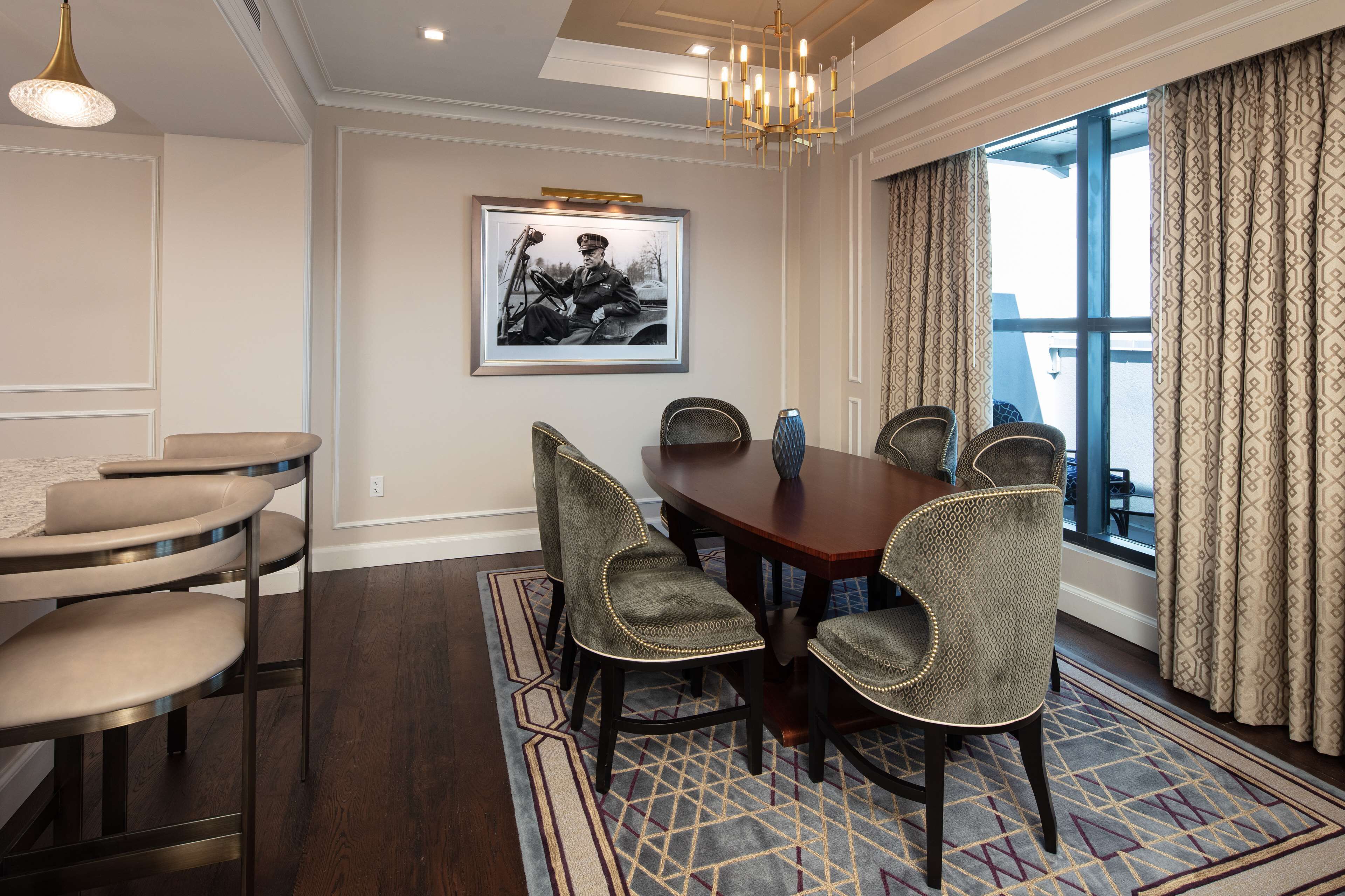 A dining area with a wooden table, six upholstered chairs, a patterned rug, and a framed photograph on the wall.