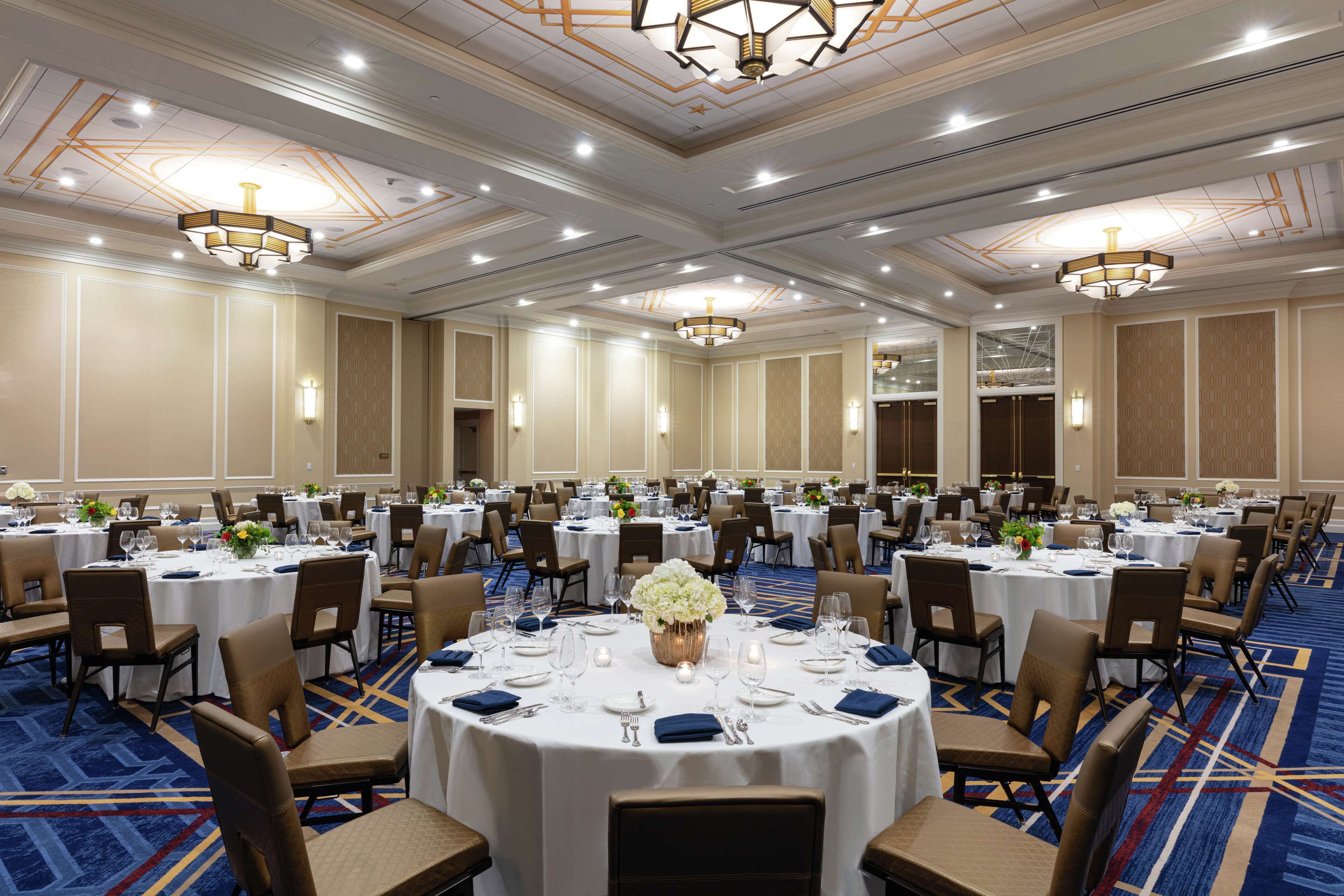 A large banquet hall with round tables, chairs, and chandeliers.