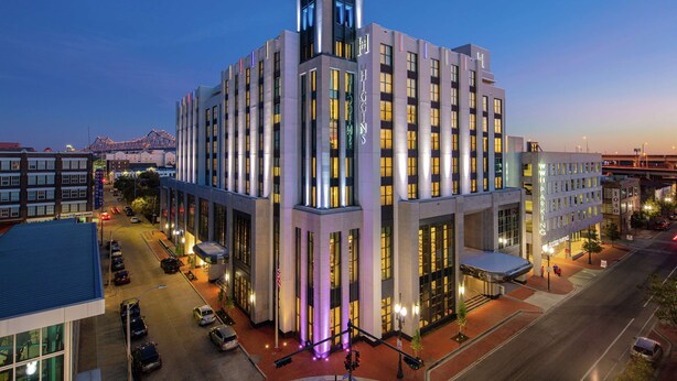A modern hotel with a prominent tower, large windows, and a parking area.