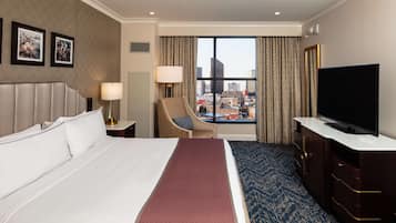 A hotel room with a large bed, a television, a desk, a chair, and a view of the cityscape.