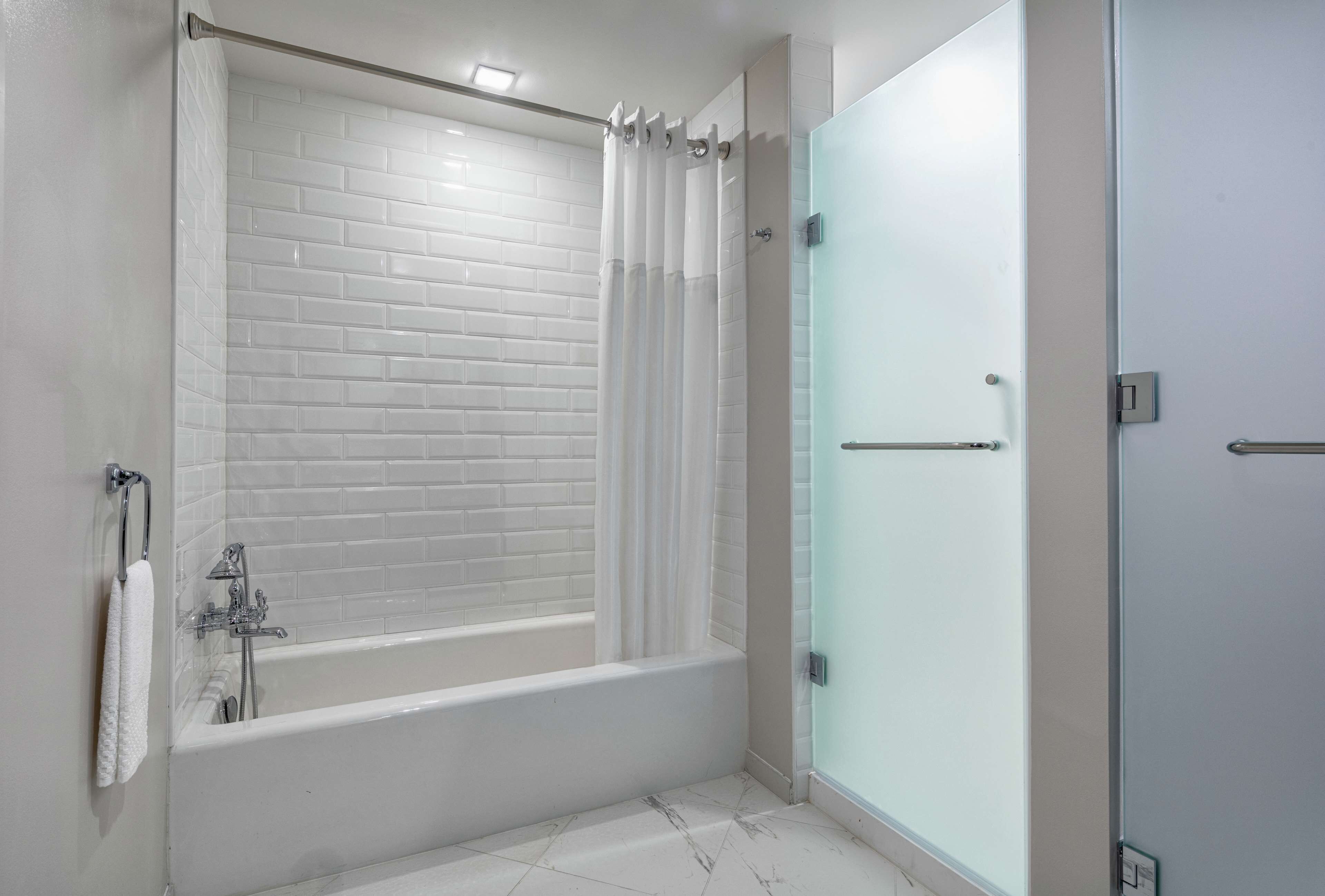 Un baño moderno con una cabina de ducha revestida de azulejos blancos, una puerta de cristal para la ducha y una bañera blanca.