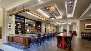 A bar area with a counter and seating, featuring a bar sign, shelves with bottles, and pendant lighting.