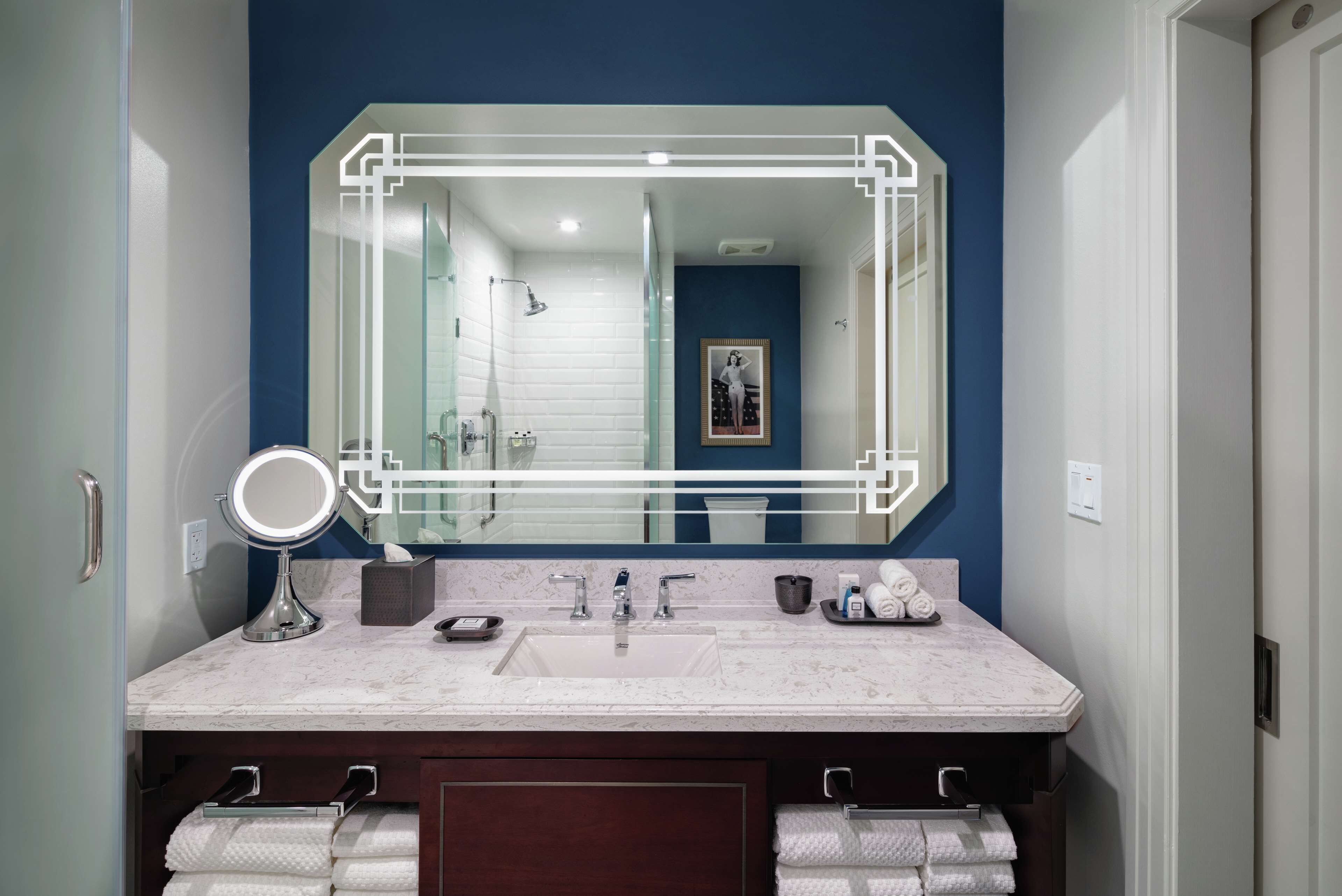 A bathroom with a large mirror, two sinks, a towel rack, and a framed picture on the wall.