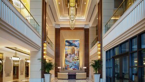 A spacious lobby with a central reception desk, a large mural, and a chandelier.
