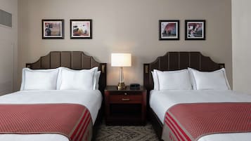 A hotel room with two beds, a nightstand with a lamp, and three framed pictures on the wall.