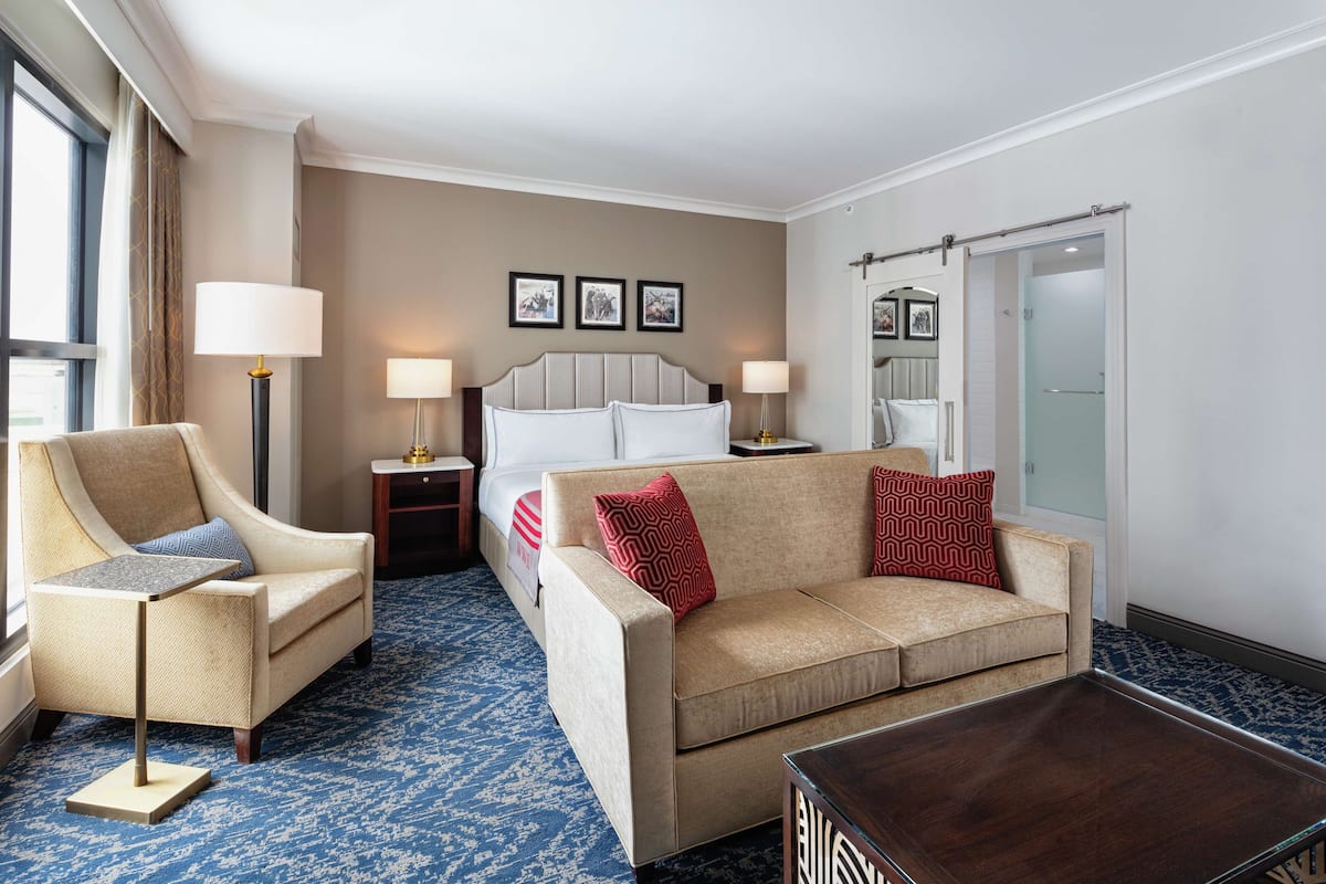 A hotel room with a bed, two sofas, a coffee table, and a lamp.
