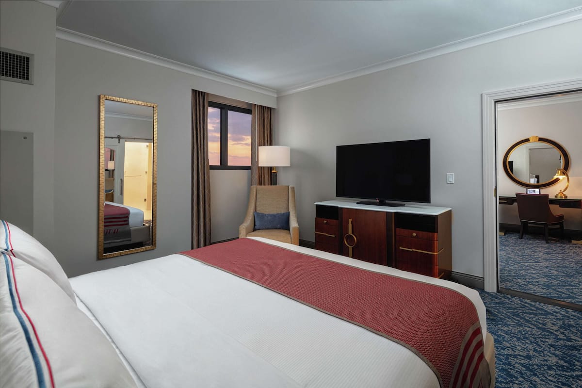 A hotel room with a large bed, a TV, a desk with a chair, and a mirror.