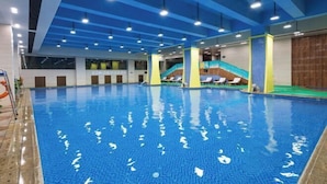 Una piscina interior con agua azul cristalina, múltiples carriles y un tobogán en el centro.