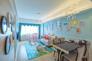 A room with a dining table, chairs, a sofa, a play area with toys, and wall art.