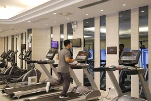A gym with treadmills and exercise equipment, a clock on the wall, and a television screen. - Minfa World Apartment Hotel Xiangyang (Zhuge Liang Square Wanda Plaza） (XIANGYANG)