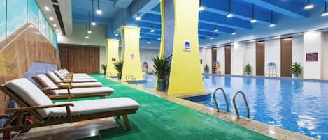 Piscina interior con múltiples tumbonas y suelo verde.
