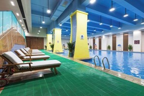 Una piscina interna con diversi lettini e pavimento verde.