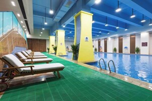 Piscina interior con múltiples tumbonas y suelo verde.