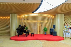 Un piano de cola sobre una alfombra roja en un escenario, con un fondo de listones verticales de madera y una planta en maceta.