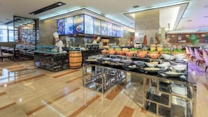 Un moderno vestíbulo de hotel con una zona de bufé que ofrece diversas opciones de comida y un área de estar con mesas y sillas.