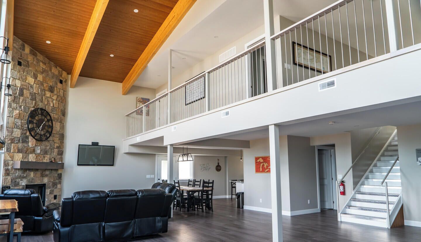 A spacious living area with a stone fireplace, a black leather couch, and a dining area with a high ceiling and a staircase.