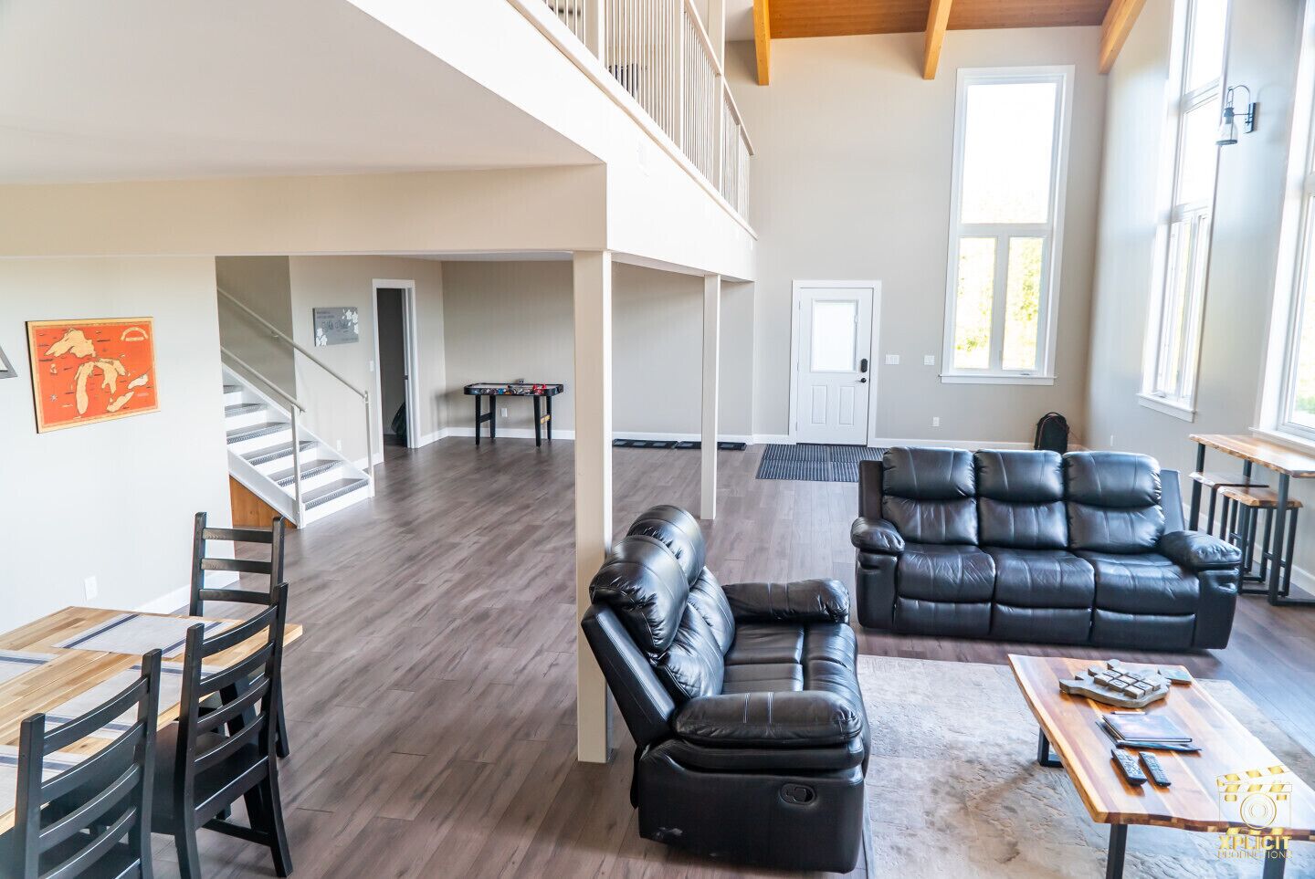 A spacious living area with a high ceiling, a black leather sofa, a wooden coffee table, and a dining table with chairs.