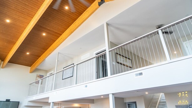 A multi-level interior with wooden beams, a balcony with white railings, and a ceiling fan.