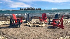 A beach with red Adirondack chairs and a fire pit.