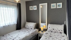 A bedroom with two beds, a large mirror, and a bedside table with a lamp.