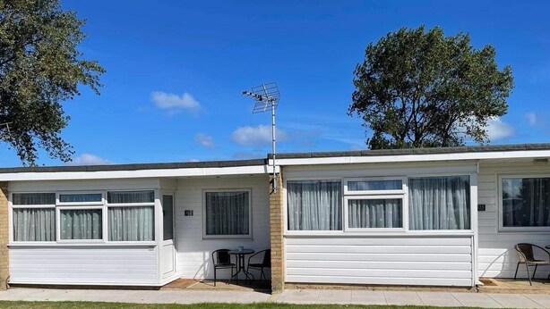 A two-story mobile home with a garage, a small patio with a table and chairs, and a satellite dish.