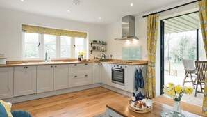 Une cuisine moderne avec des armoires blanches, un plan de travail en bois et un four encastré. Une fenêtre est agrémentée d’un rideau à motifs floraux jaunes, et offre une vue sur le jardin.