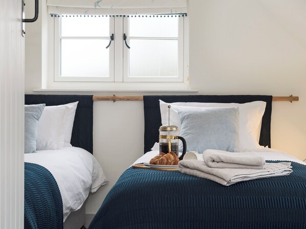 A bedroom with two beds, a window with curtains, a coffee maker, and a croissant on the bed.