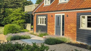 Une maison à deux étages avec une façade en briques, un toit en tuiles et un petit jardin devant, agrémenté de plantes de lavande.