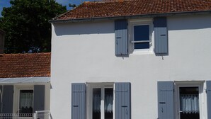 Um edifício branco com persianas azuis, telhado em telhas e porta branca.