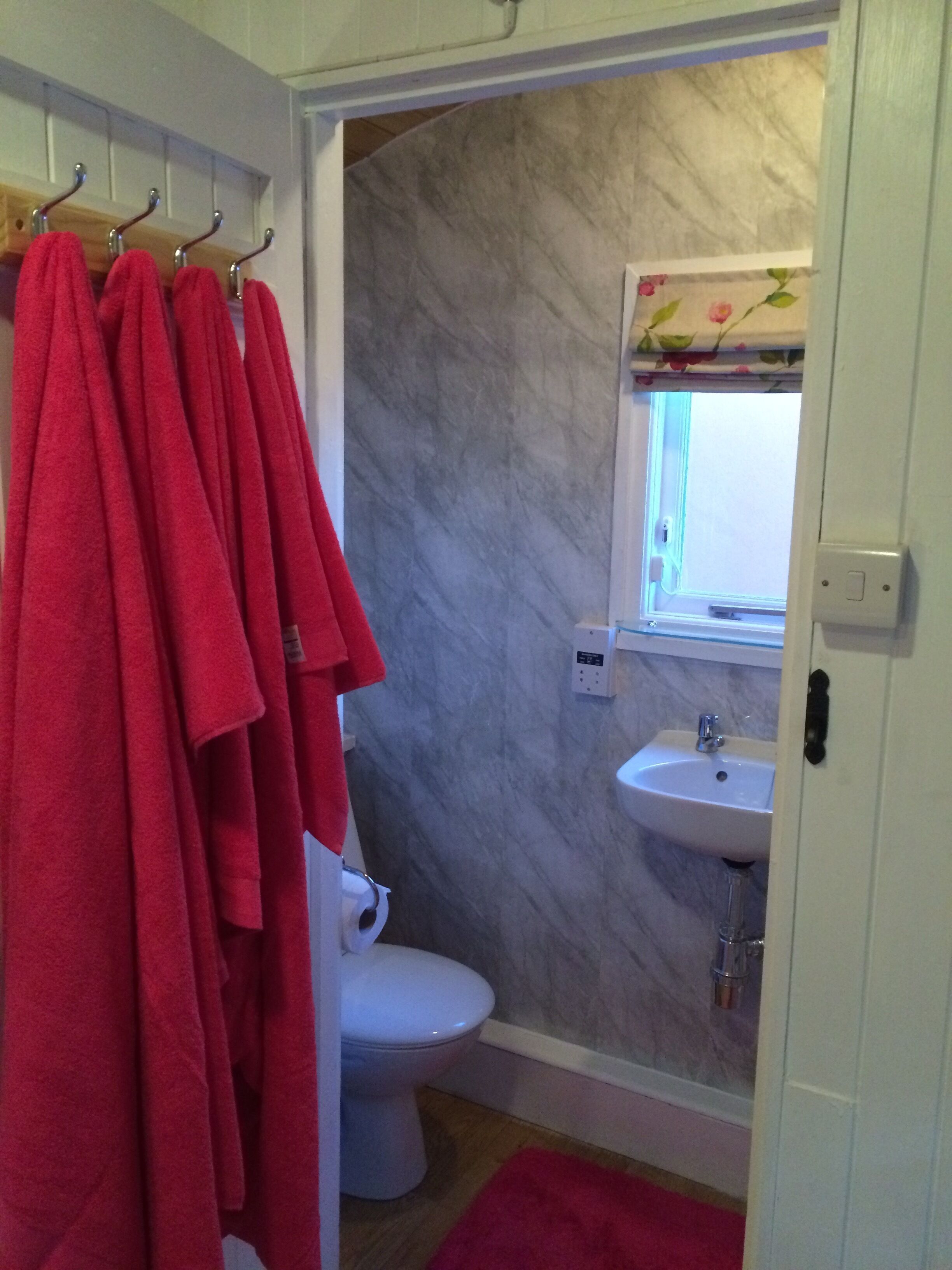 Ein Badezimmer mit Toilette, Waschbecken und Duschbereich mit roten Handtüchern.