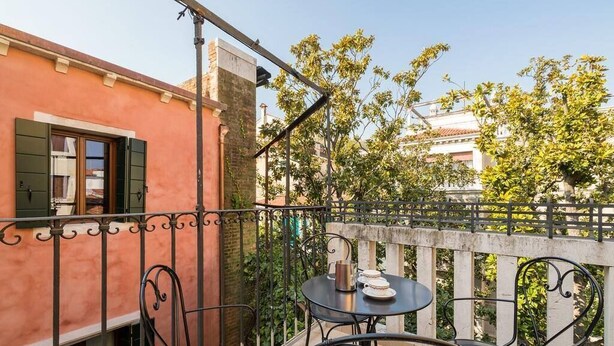 A balcony with a table and chairs, a window with shutters, and a view of buildings and trees. - Le Terrazze apartment, on two floors (Unknown)