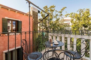 A balcony with a table and chairs, a window with shutters, and a view of buildings and trees. - Le Terrazze apartment, on two floors (Unknown)